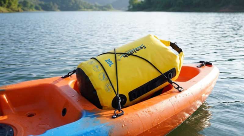 Yellow semi-circular kayak dry backpack strapped into the tank well of a sit-on-top kayak with bungees